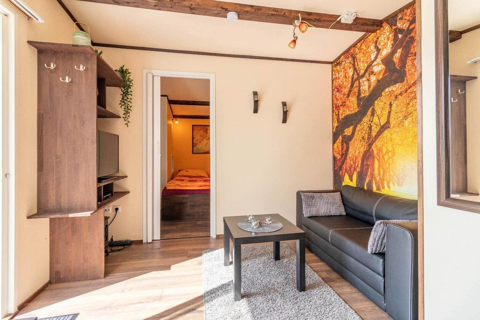 Wohnbereich mit Sofa, Couchtisch und Wandbild. Im Hintergrund ist ein Schlafzimmer sichtbar.