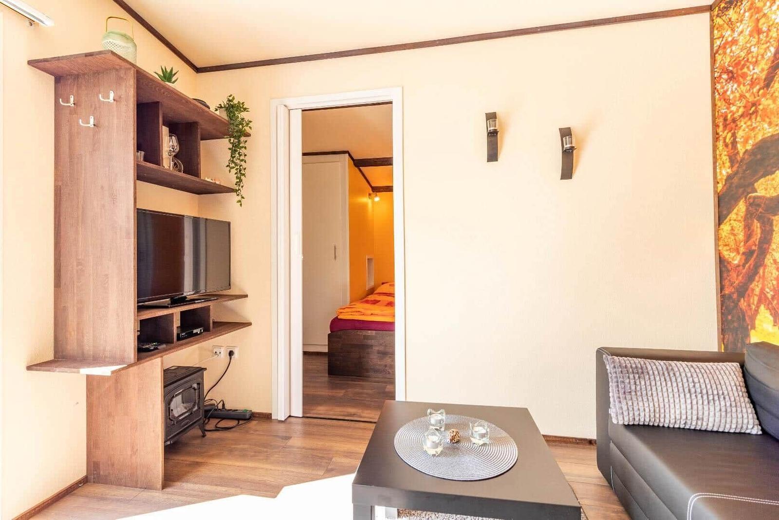 Wohnzimmer mit Sofa, Couchtisch und Fernseher. Durchgang zur Schlafzimmer.