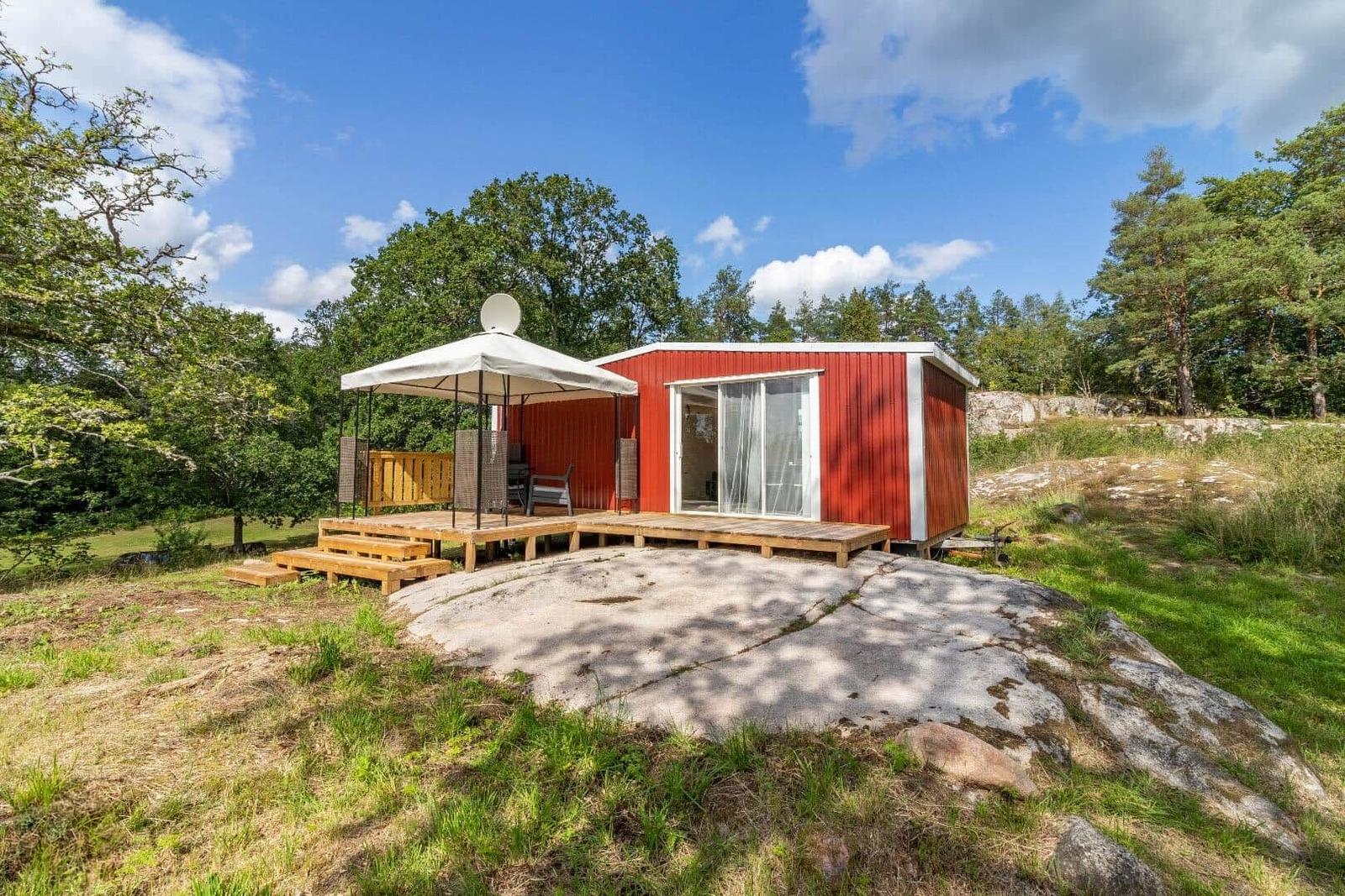 Rotes Holzhaus mit Terrasse und Sonnensegel in grüner Umgebung.