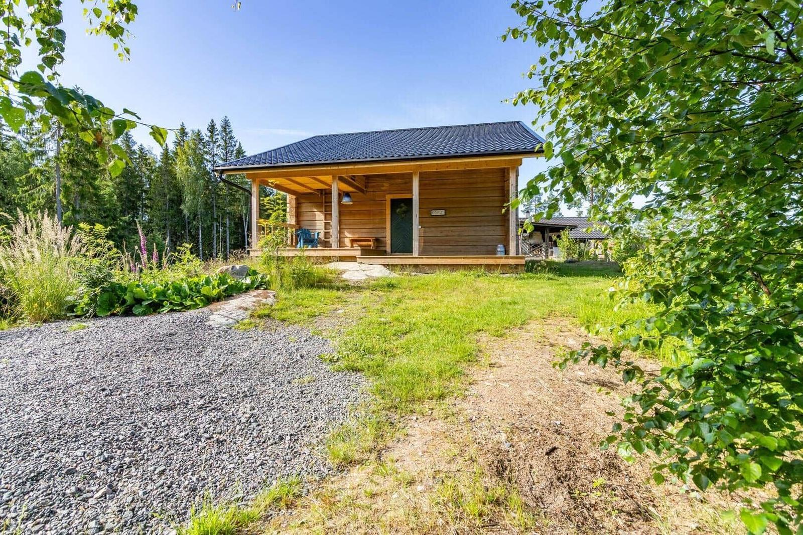 Wooden cabin with porch, surrounded by forest and greenery.
