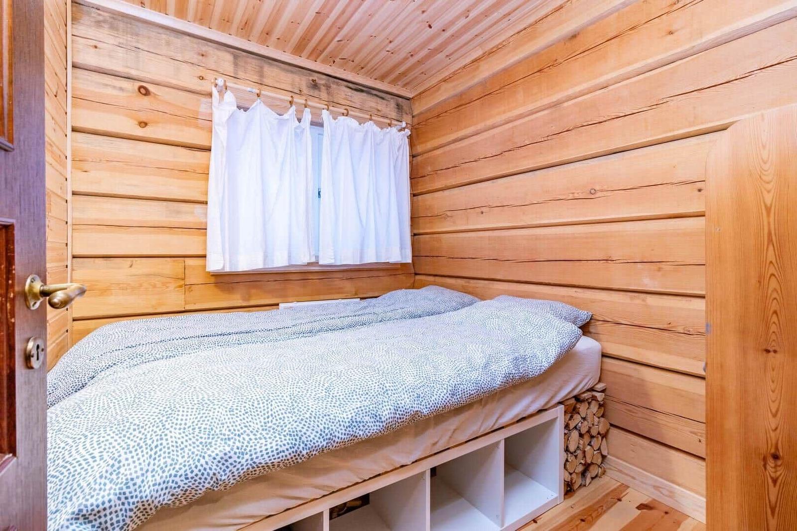 Bedroom with wooden walls, bed, and window with white curtains.