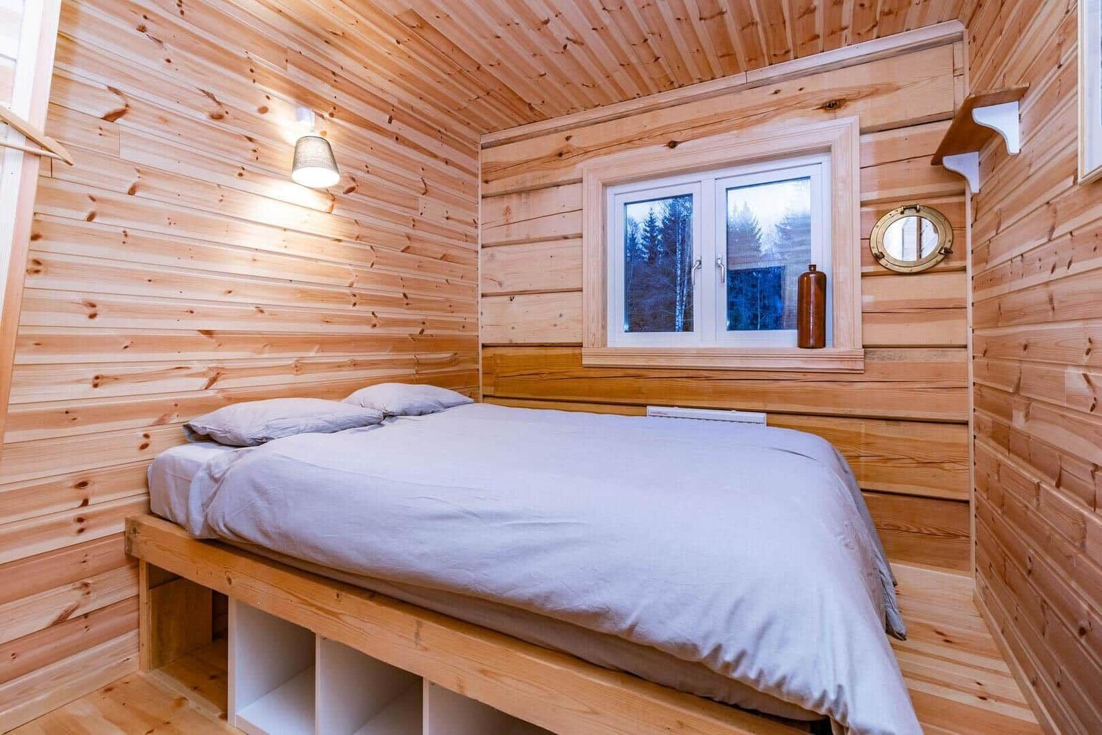 Bedroom with wooden walls, bed, and window with view of forest.