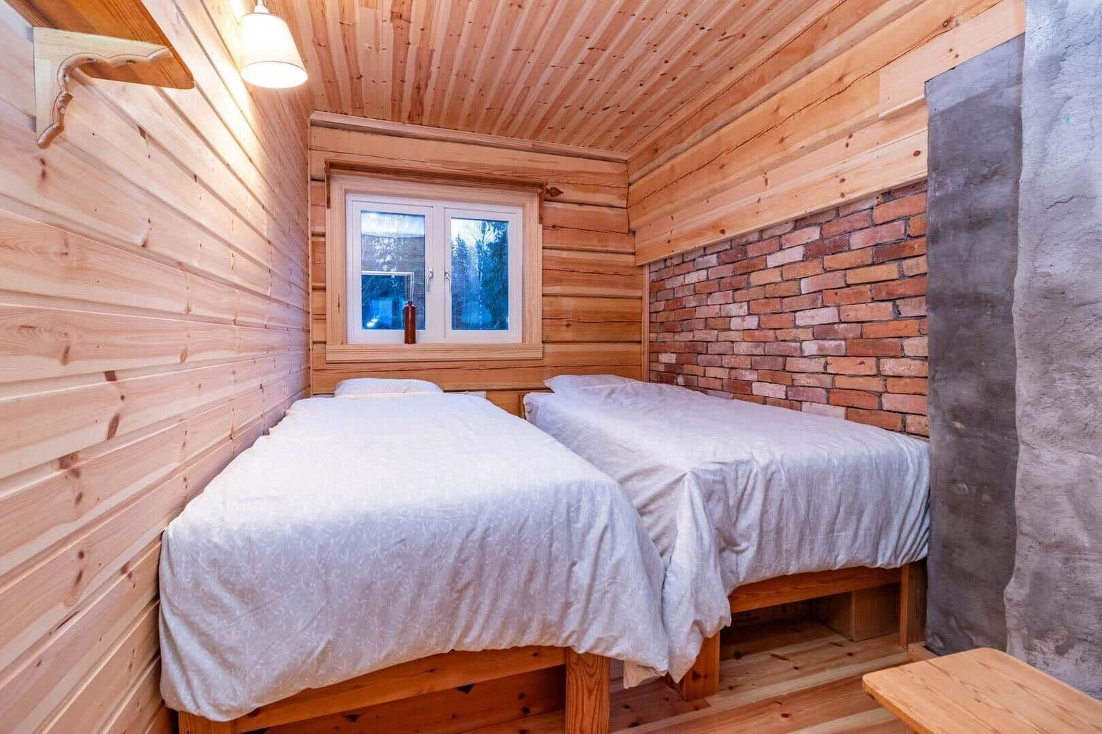 Two beds in a room with wood wall and brick wall.