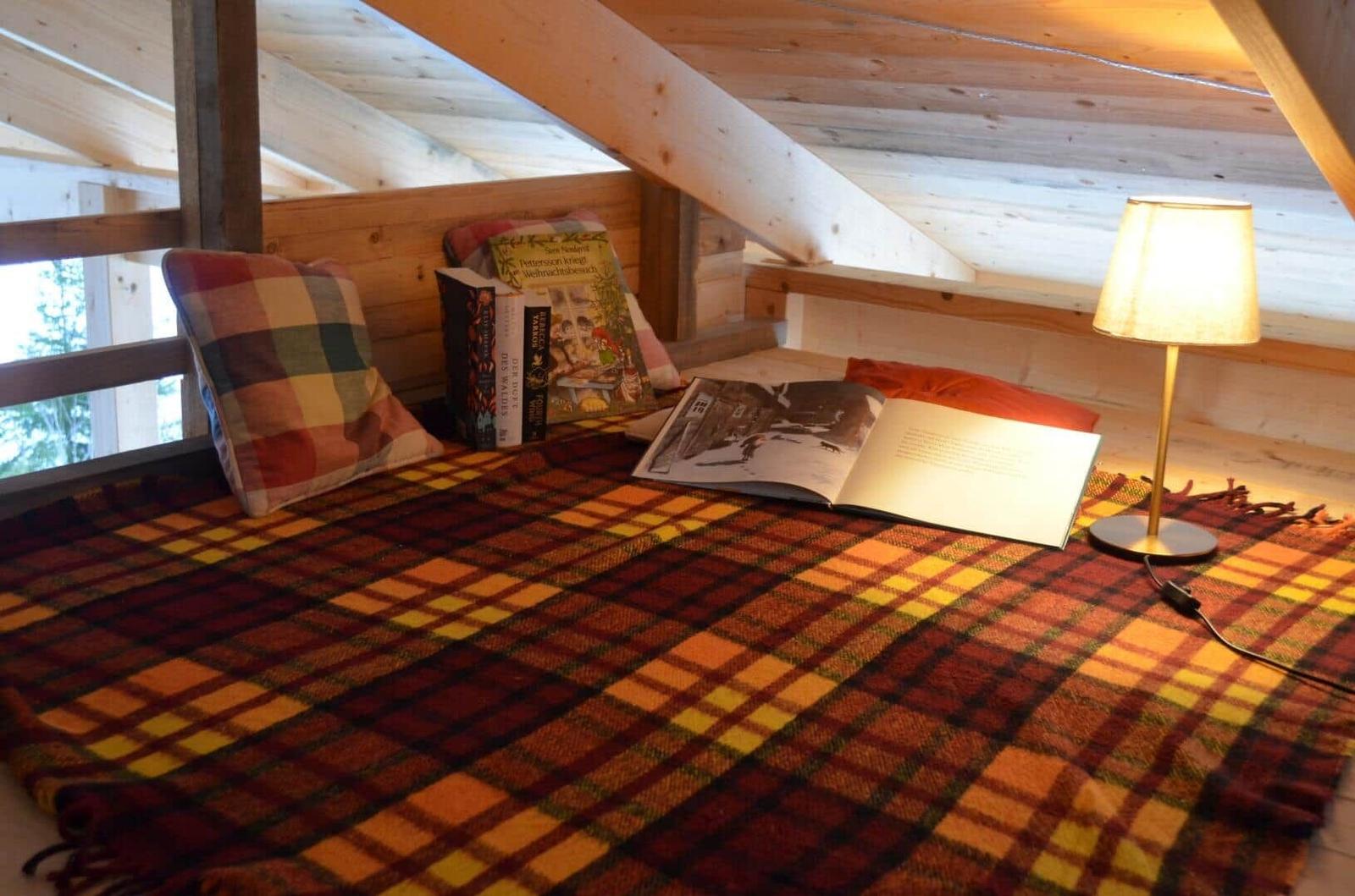 A loft bed with a blanket, pillows, and a lamp.