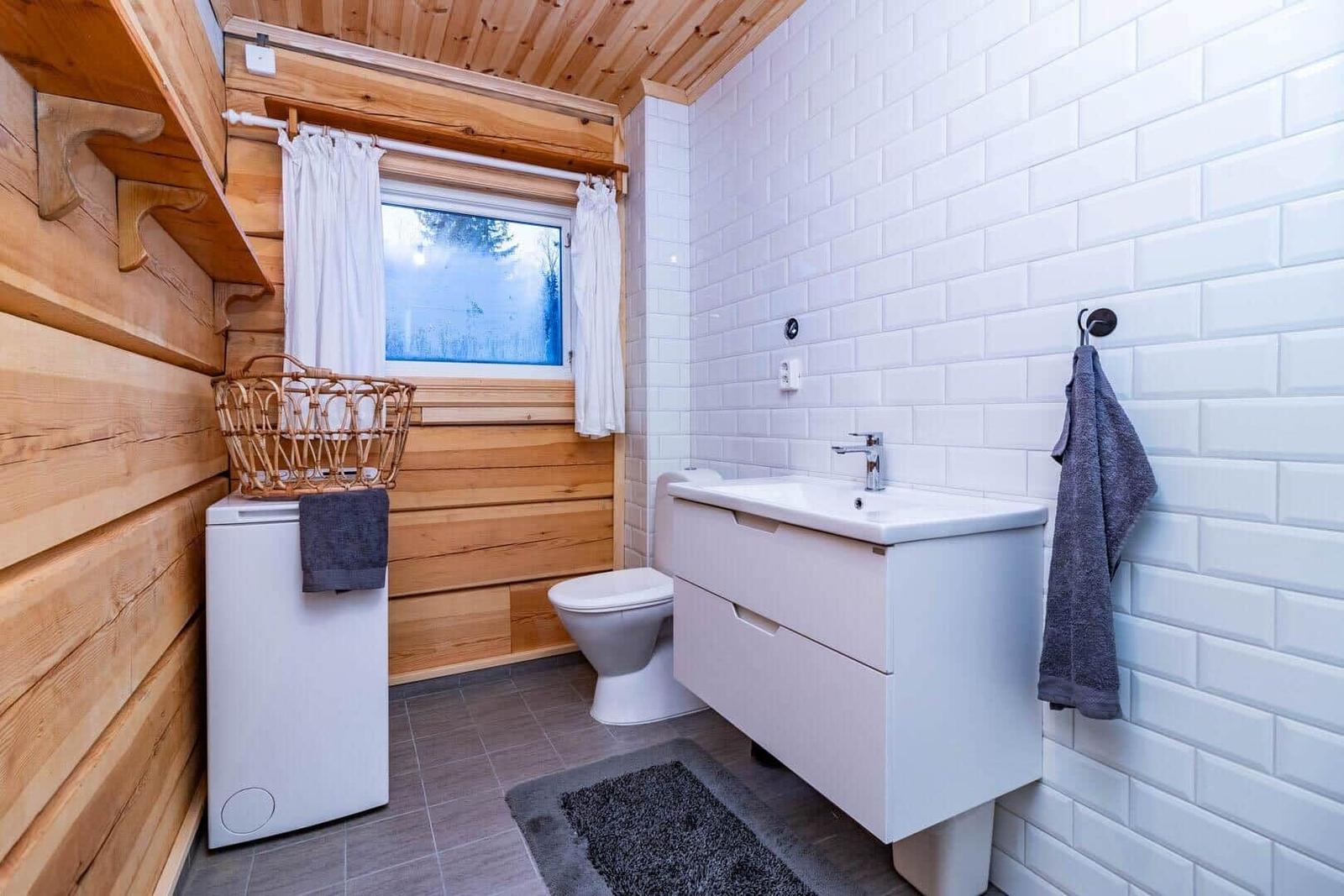 Bathroom with sink, toilet, and window with wooden wall.