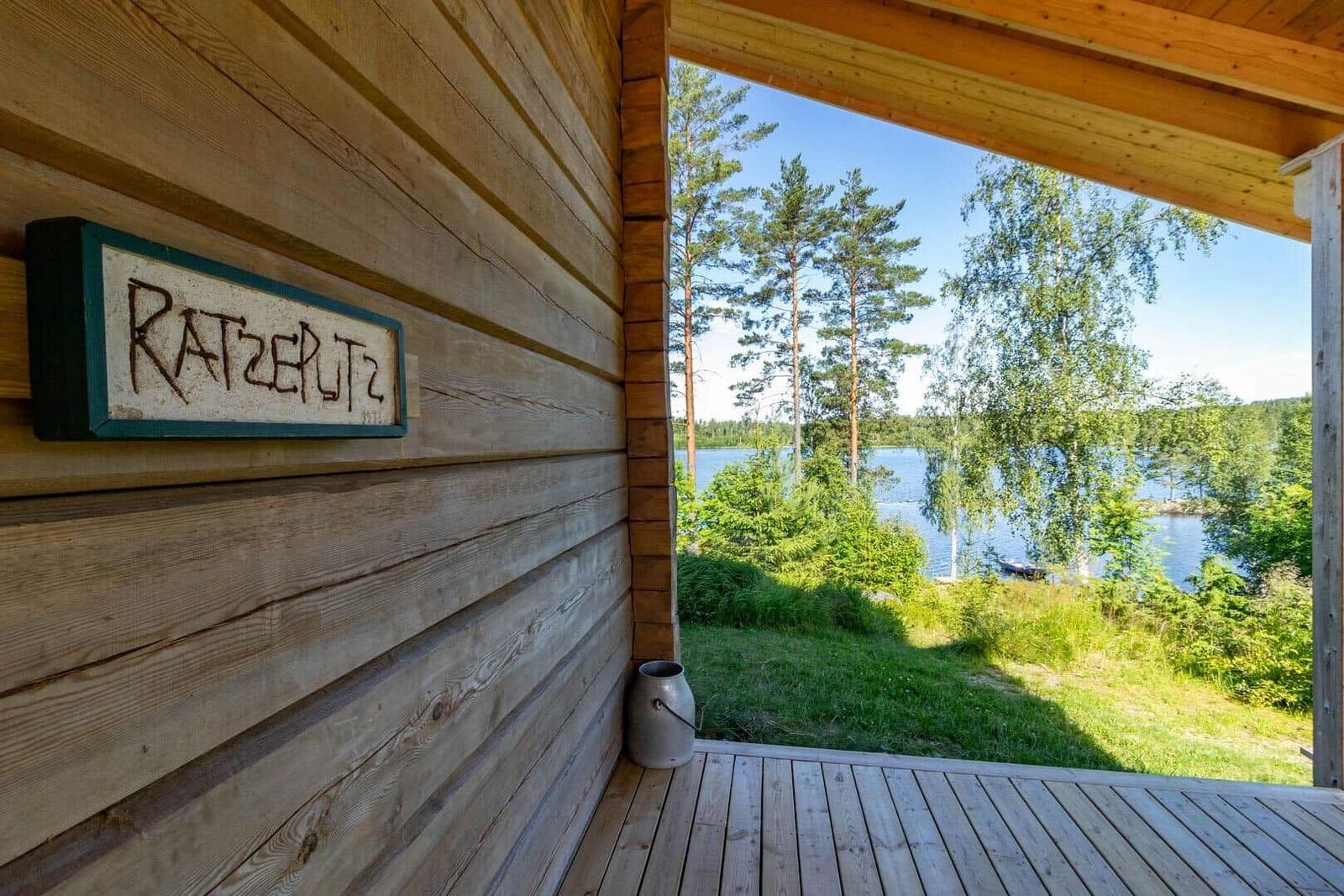 Wooden house with sign RATZERLITZ and view of lake and trees.