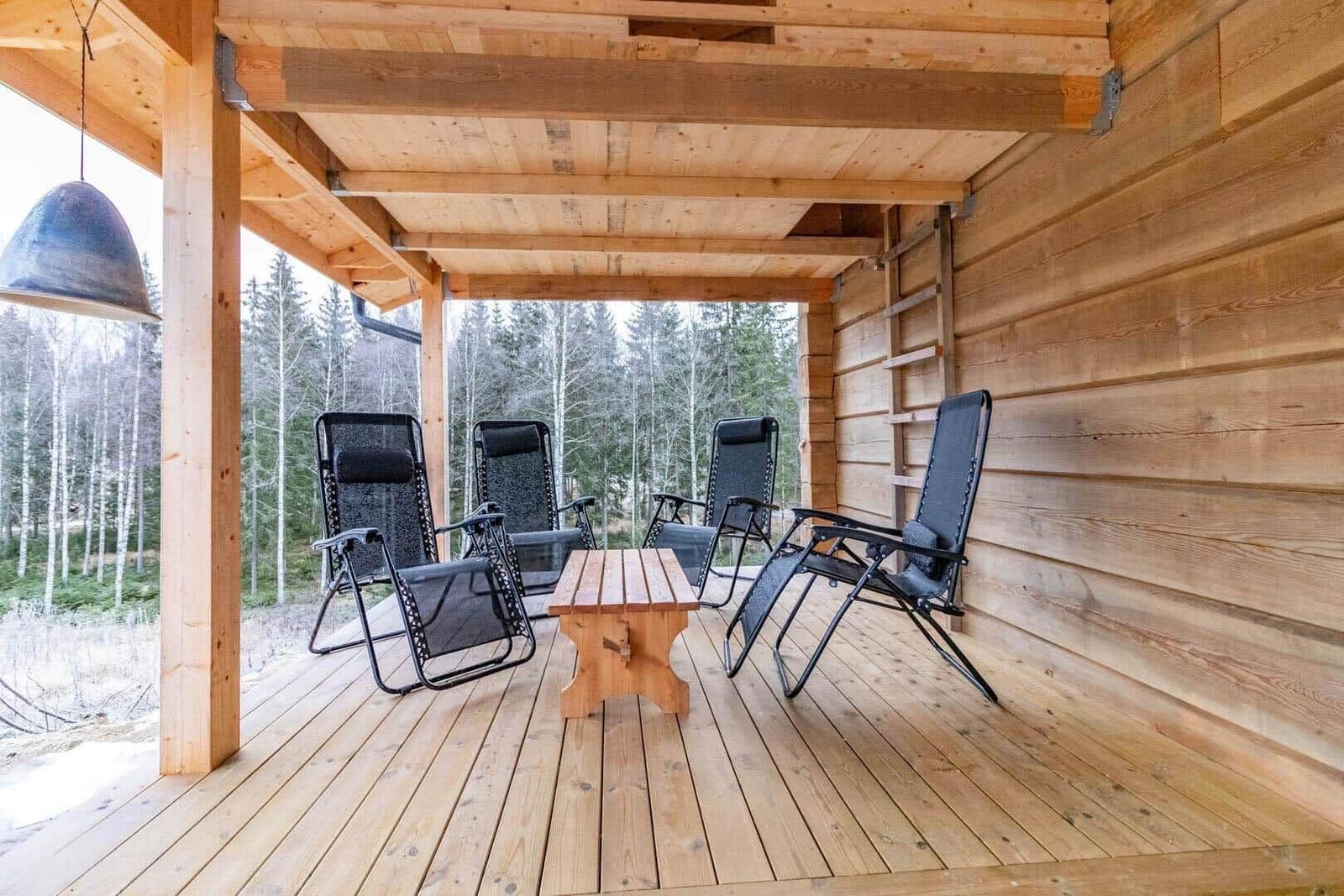 Wooden terrace with four lounge chairs and table. View of forest in background.