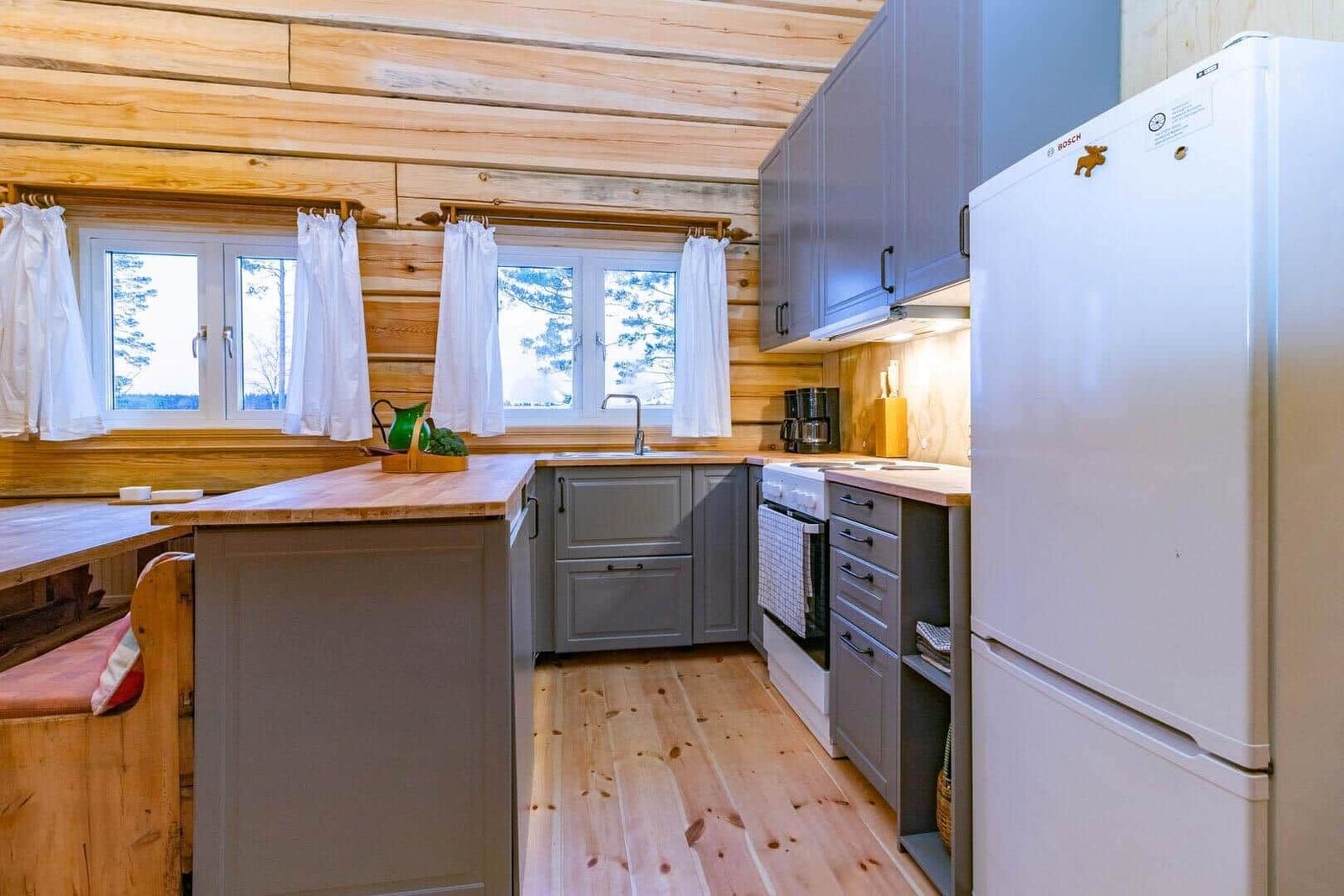 Kitchen with wooden walls, windows, worktop, and refrigerator.