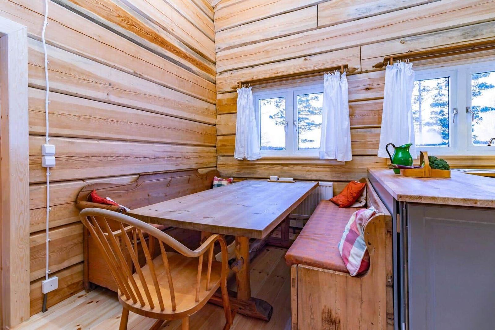 Dining area with wooden table, bench seating, and windows with white curtains.