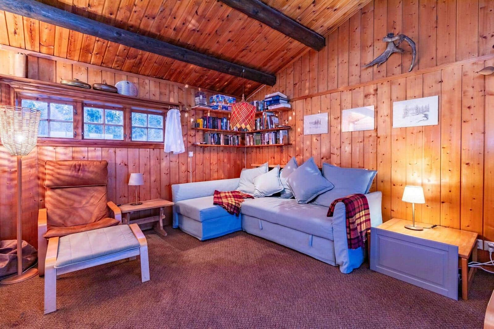 Living room with sofa, armchair, and bookshelf against wood wall.