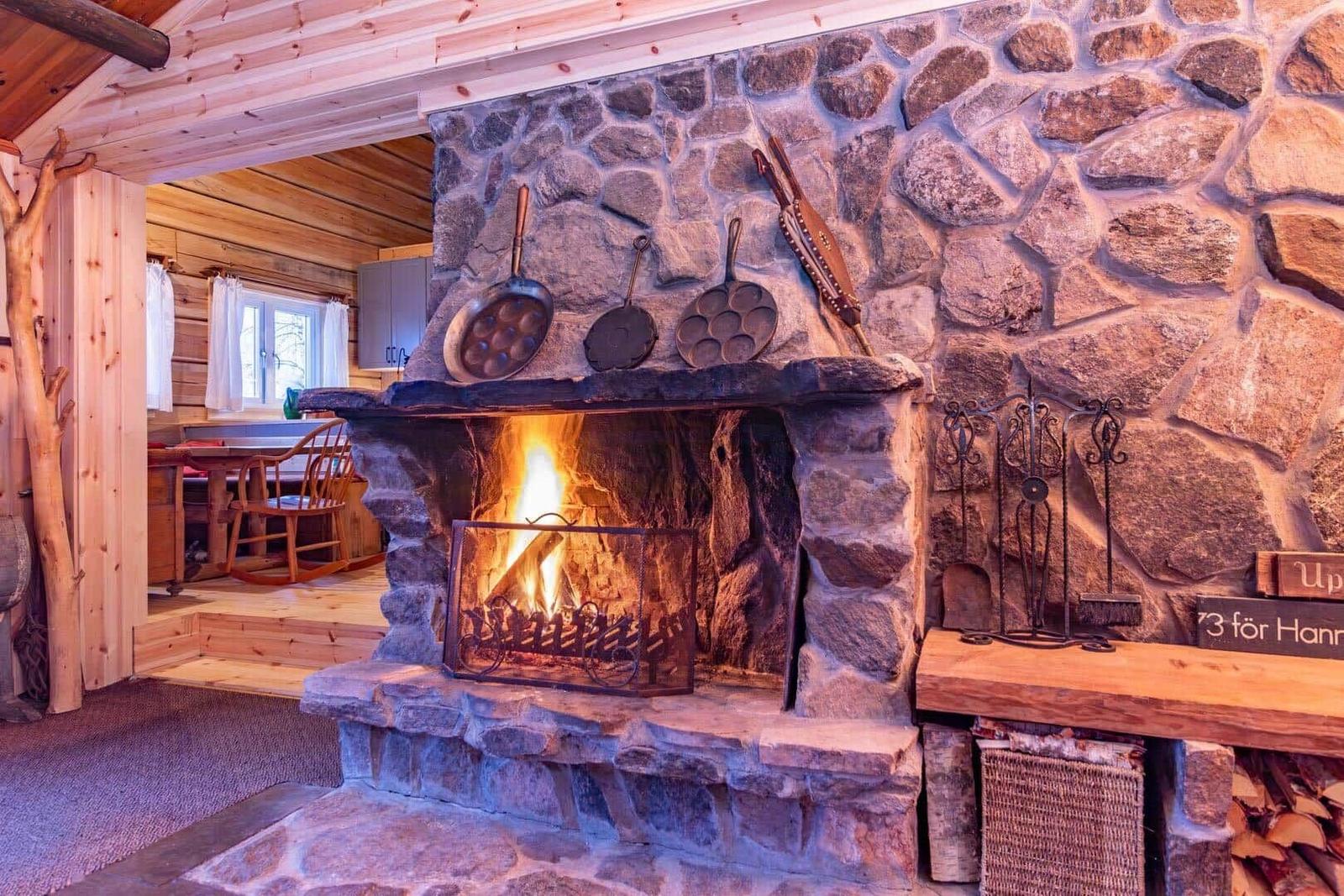 Stone fireplace with burning fire, above hanging pans and tools.