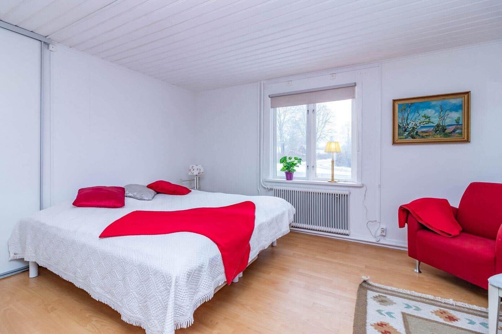 Schlafzimmer mit Bett, rotem Sofa und Fenster mit Blick.