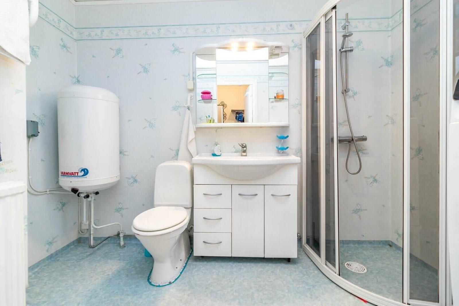 Badezimmer mit Dusche, Waschbecken und Toilette. Wandverkleidung mit Muster.