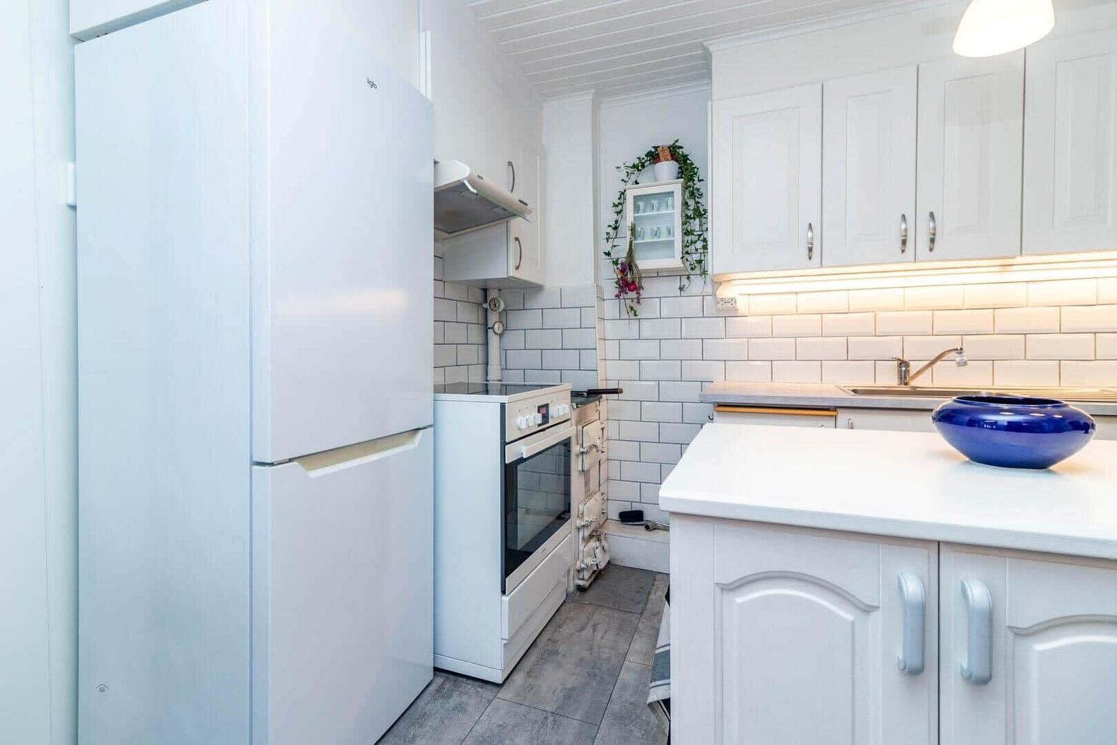Küche mit weißen Schränken, Kühlschrank und Herd. Fliesenwand und Arbeitsplatte.