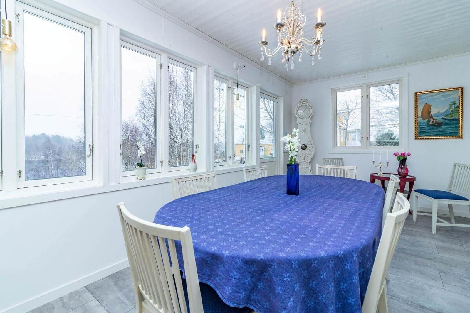 Esszimmer mit blauem Tischdecken, weißen Stühlen und großen Fenstern.