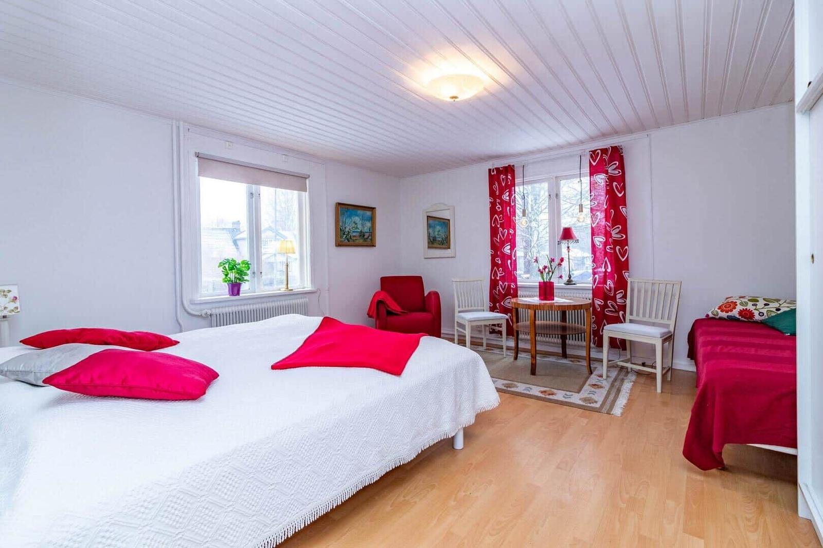 Ein Schlafzimmer mit Doppelbett, kleinem Bett, roten Vorhängen und Holzboden.