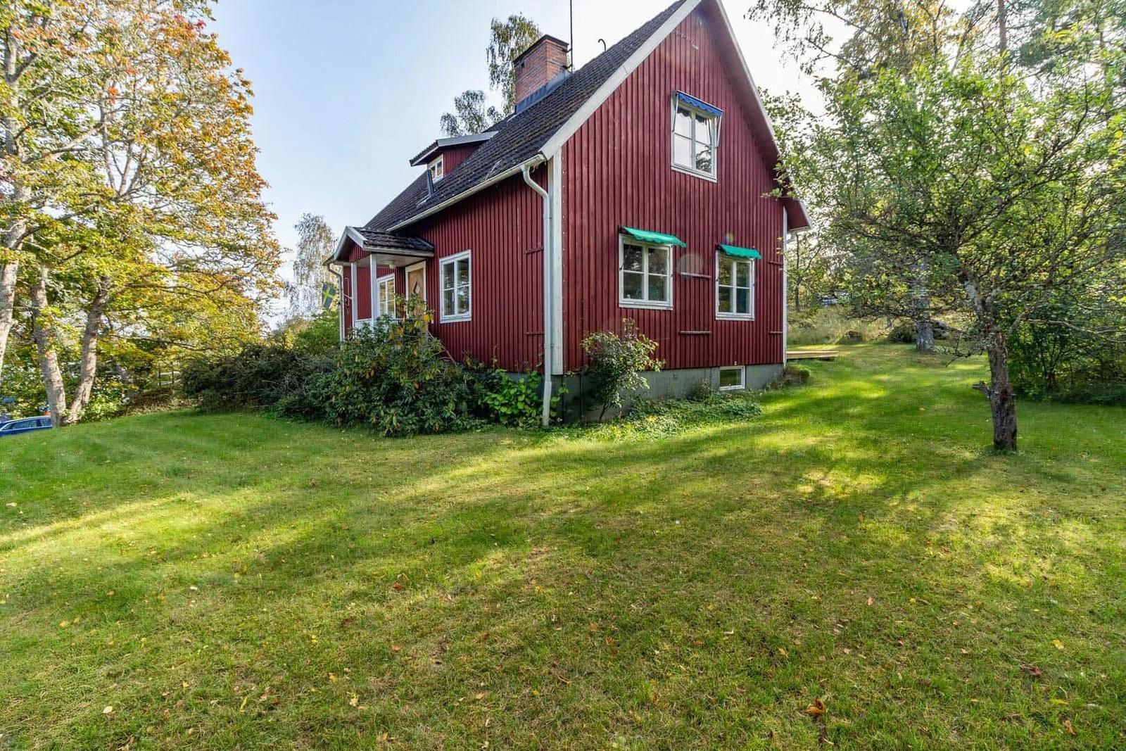 Rotes Holzhaus mit grünem Grundstück und Bäumen.