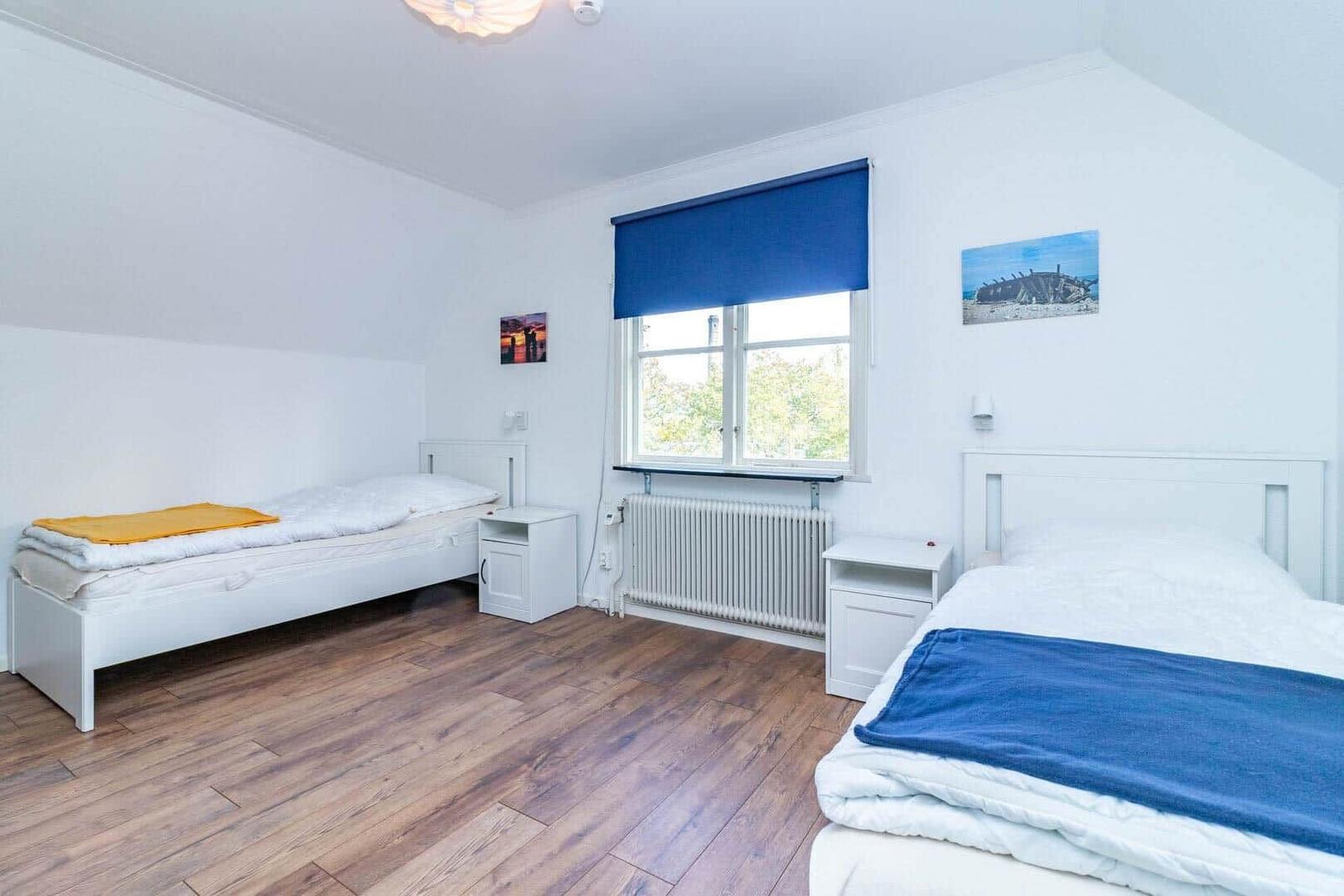 Zwei Betten, Fenster mit blauem Rollladen, Holzboden und Wandbilder.