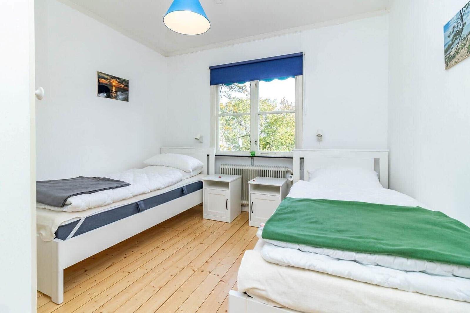 Zwei Einzelbetten mit weißen Laken und Decken in einem Raum mit Holzboden und Fenster.