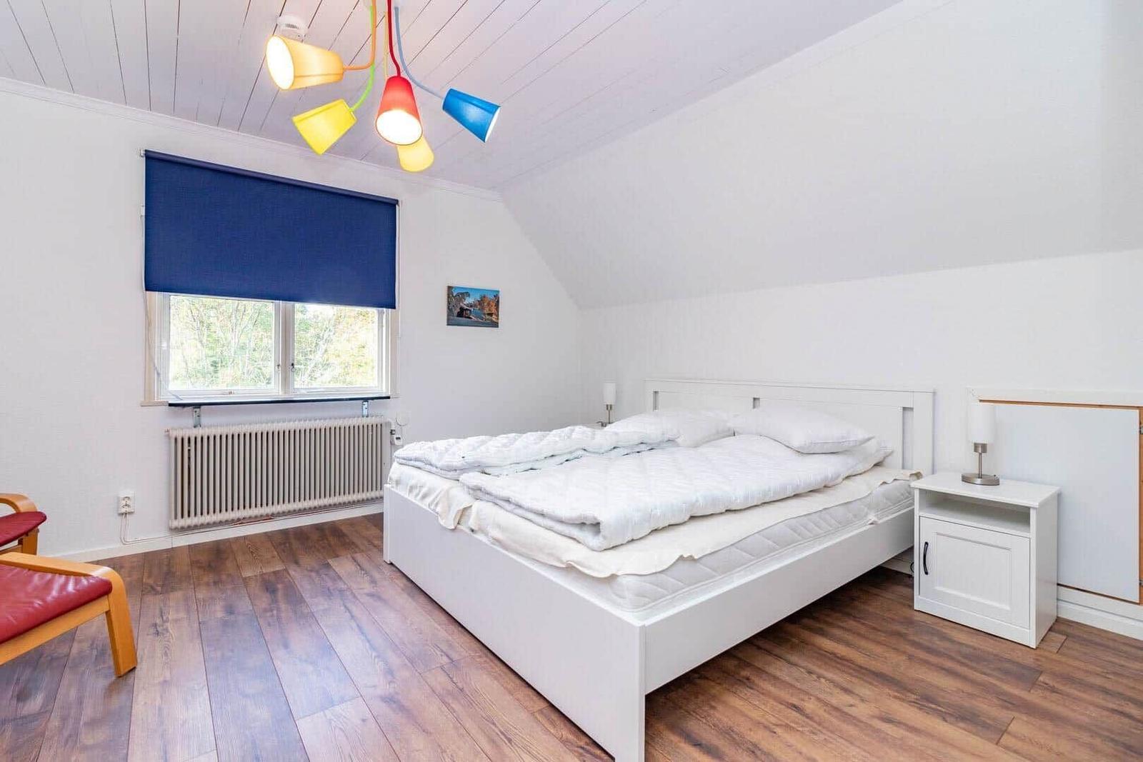 Schlafzimmer mit weißem Bett, Holzboden und farbiger Deckenleuchte.
