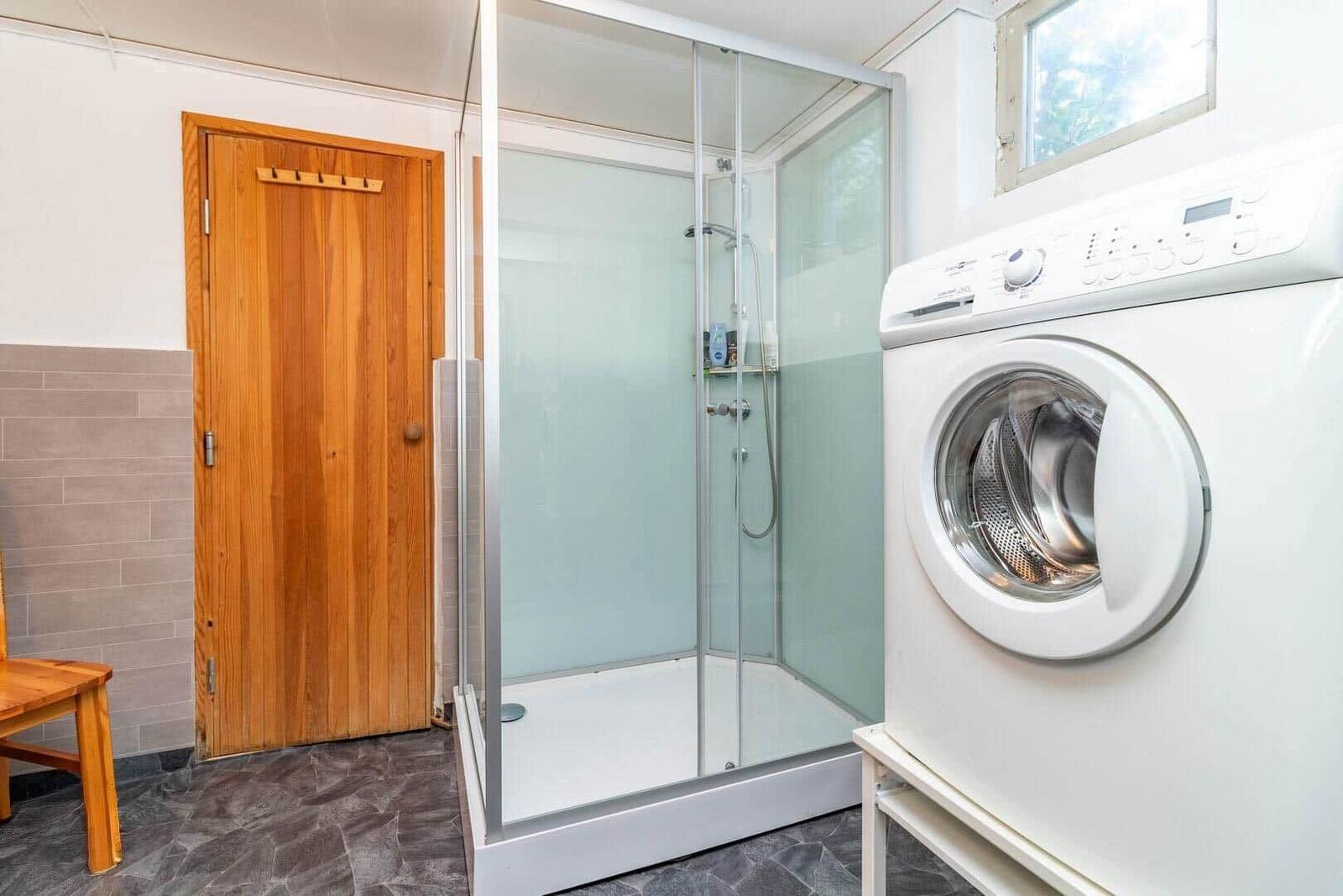 Dusche mit Glaswand, Waschmaschine und Holztür im Bad.