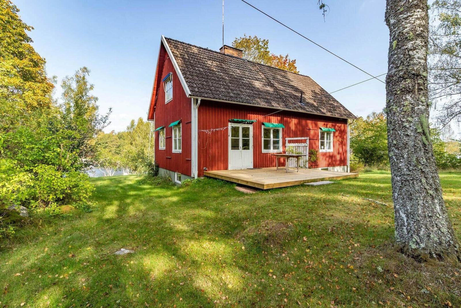 Rotes Holzhaus mit Terrasse und grünem Garten. Fenster mit grünen Markisen.