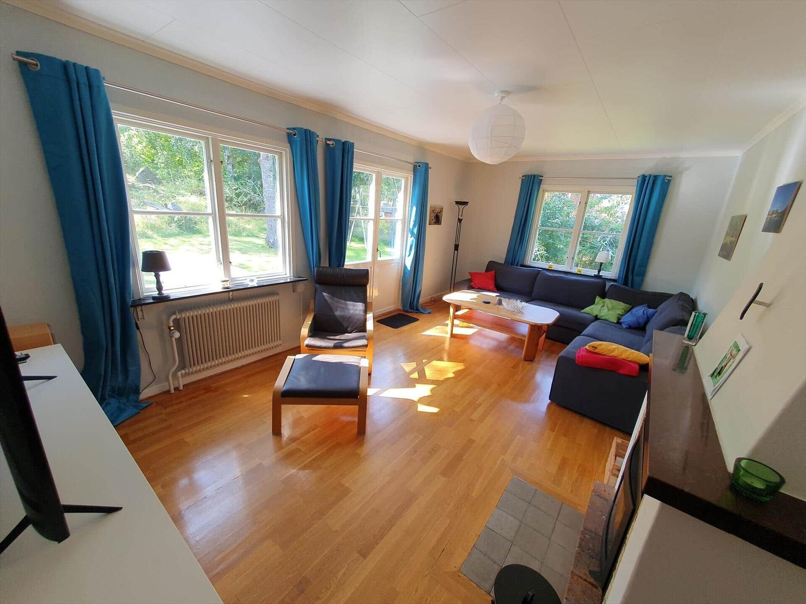 Wohnzimmer mit Sofa, Sessel und Holzboden. Fenster mit blauen Vorhängen.