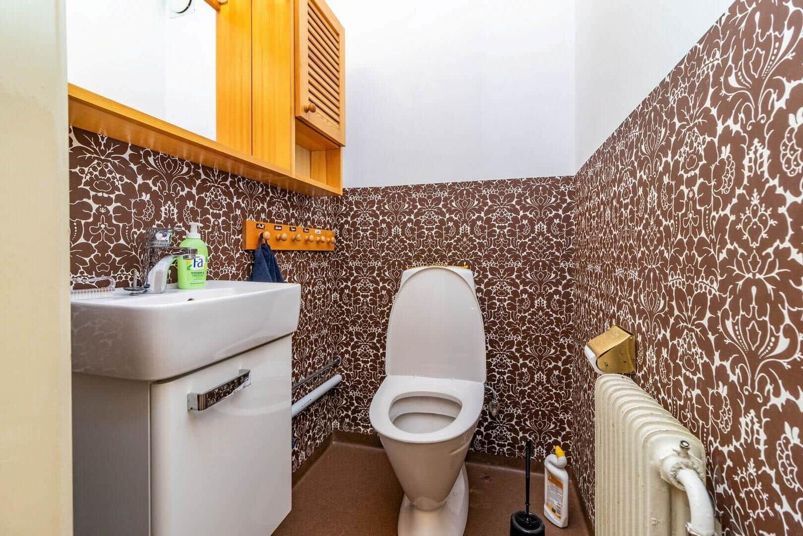 Badezimmer mit Toilette, Waschbecken und braun-weißem Tapetenmuster an den Wänden.