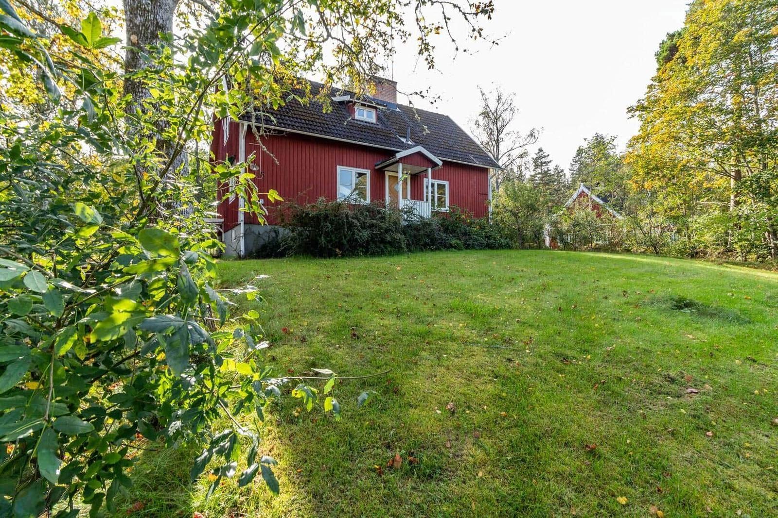 Rotes Haus mit grünem Garten und Bäumen im Hintergrund.