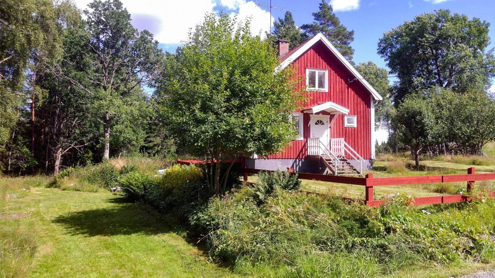 Rotes Holzhaus mit weißem Vordach und Treppenhaus. Umgeben von Bäumen und Gras.
