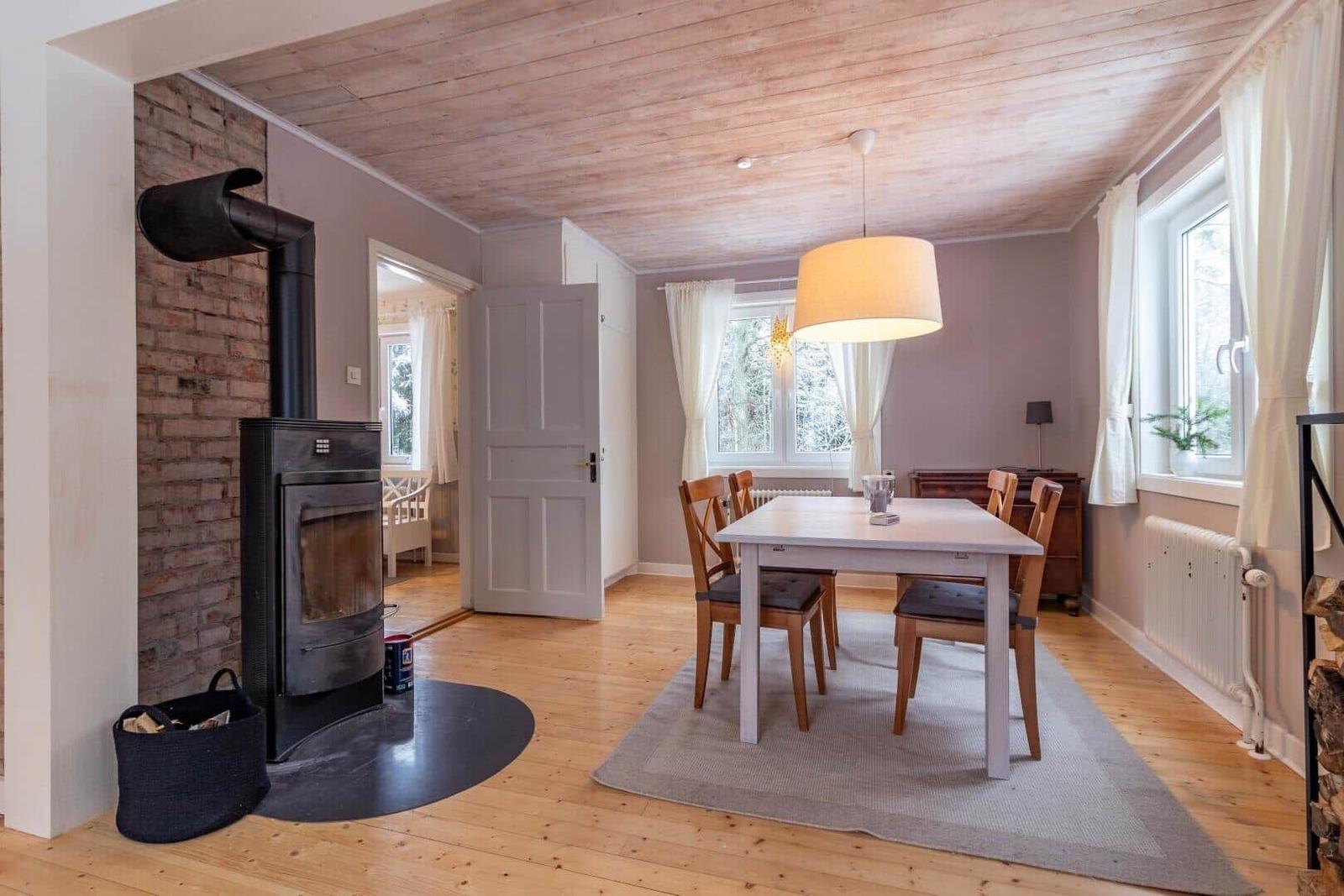 Esszimmer mit Holzboden, Tisch, Stühle und Kaminofen an der Wand.