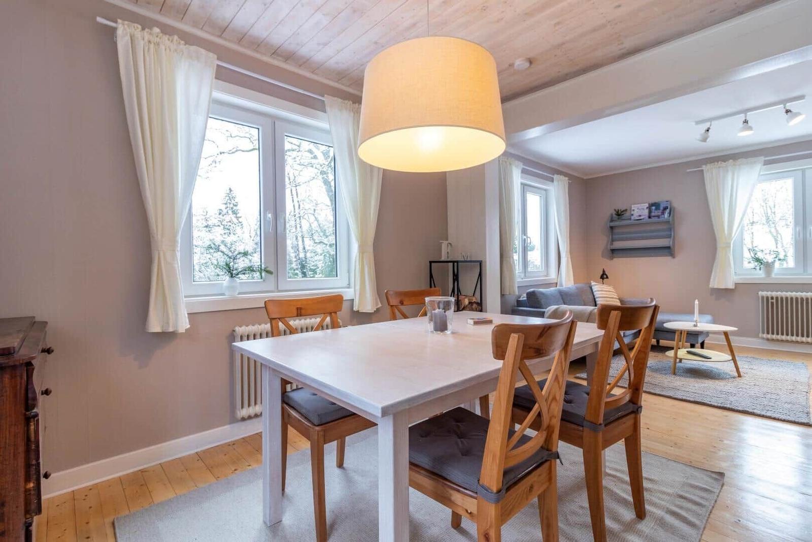 Essbereich mit Tisch und Stühlen, Wohnbereich mit Sofa und Fenstern.