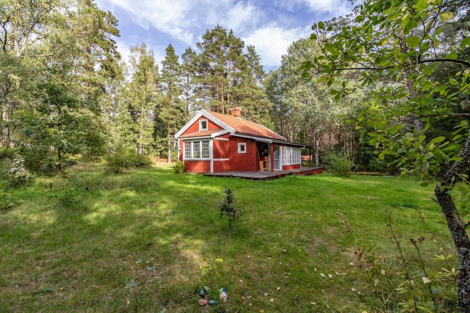 Red wooden house with terrace in the woods. Lawn and trees surround the accommodation.