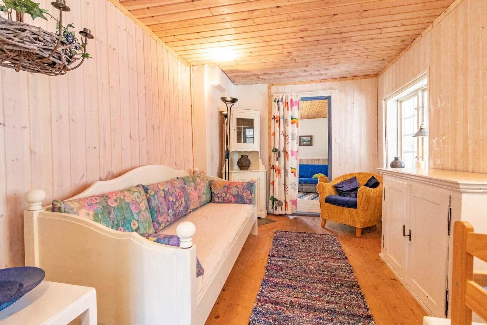 Living room with sofa, armchair, and wood-paneled walls. Hallway to another room.