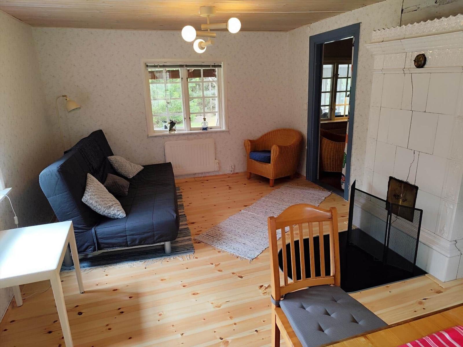 Living room with sofa, armchair, and fireplace. Wooden floor and window with view outside.
