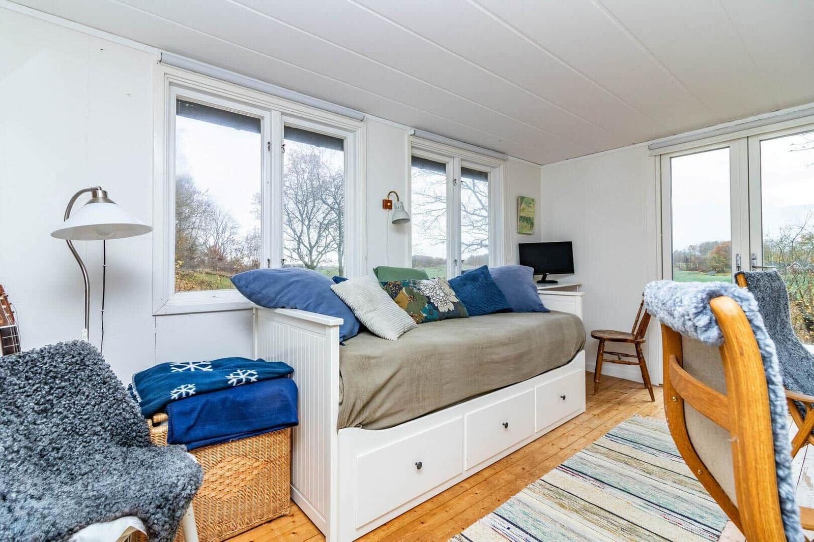 Schlafzimmer mit Bett, Fenstern und Stuhl. Holzboden und weiße Wände.