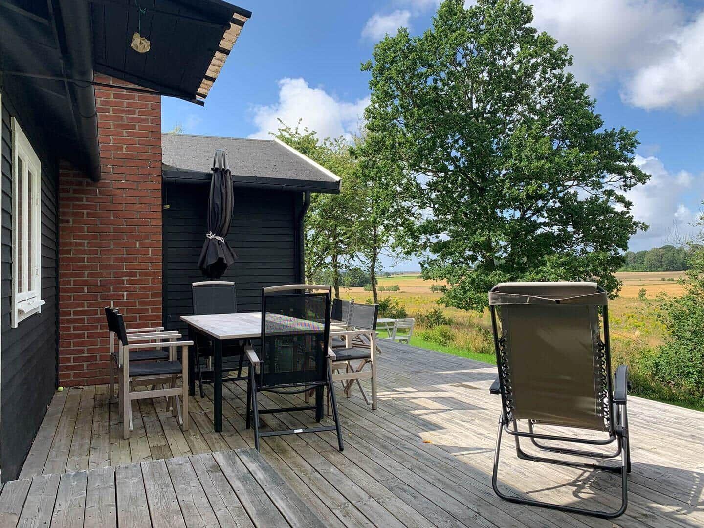 Terrasse mit Tisch, Stühlen und Liegestuhl. Blick auf Felder und Bäume.