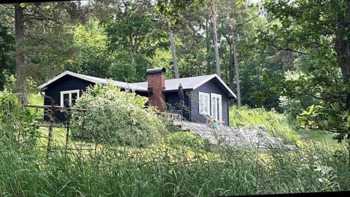 Schwarze Holzhütte mit rotem Schornstein im Wald. Eingangstreppe und Fenster mit weißen Rahmen.
