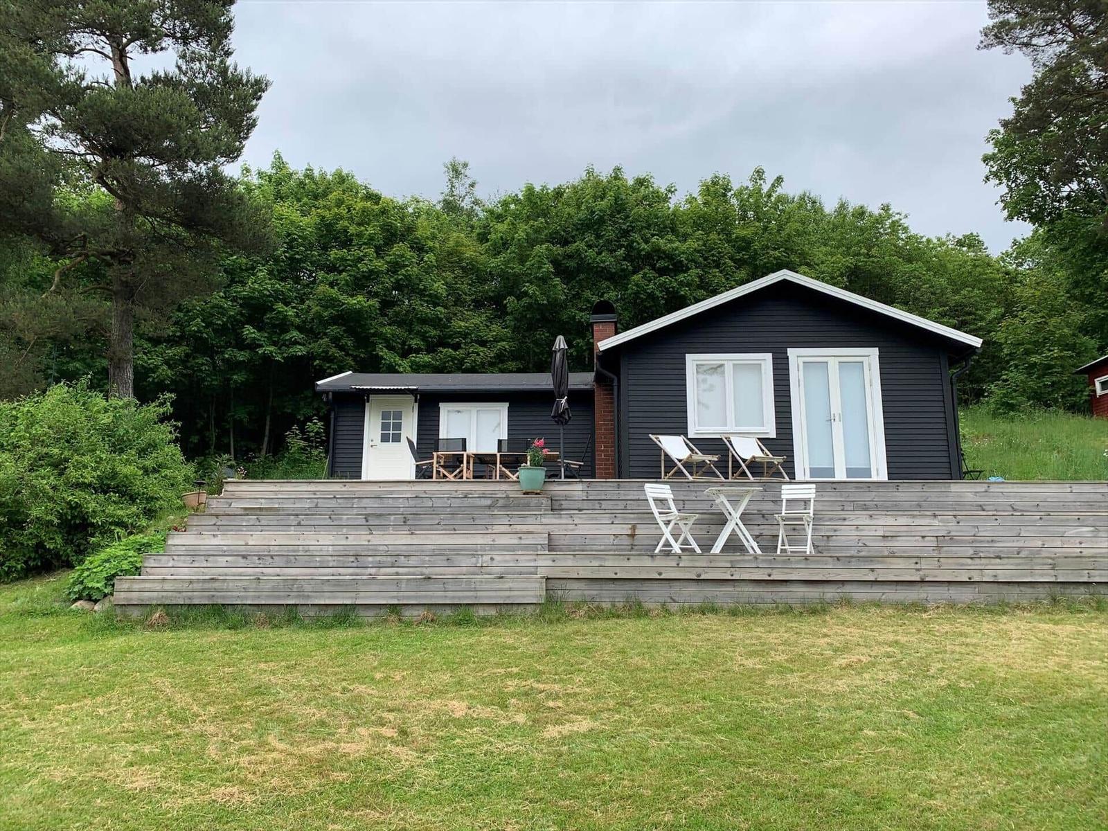 Schwarze Hütte mit Terrasse, Garten und Bäumen im Hintergrund.