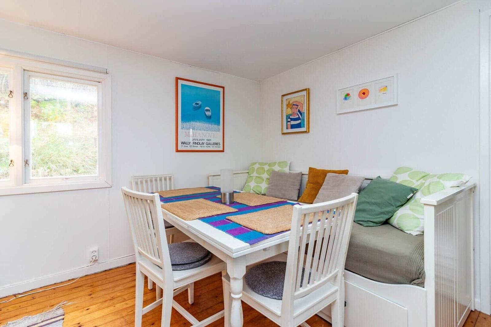 Essbereich mit Tisch, Stühlen und Sofa. Fenster und Wandbilder sind sichtbar.