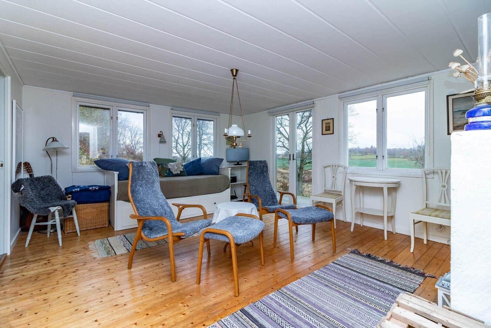 Wohnraum mit Holzboden, Fenstern und blauen Sesseln.