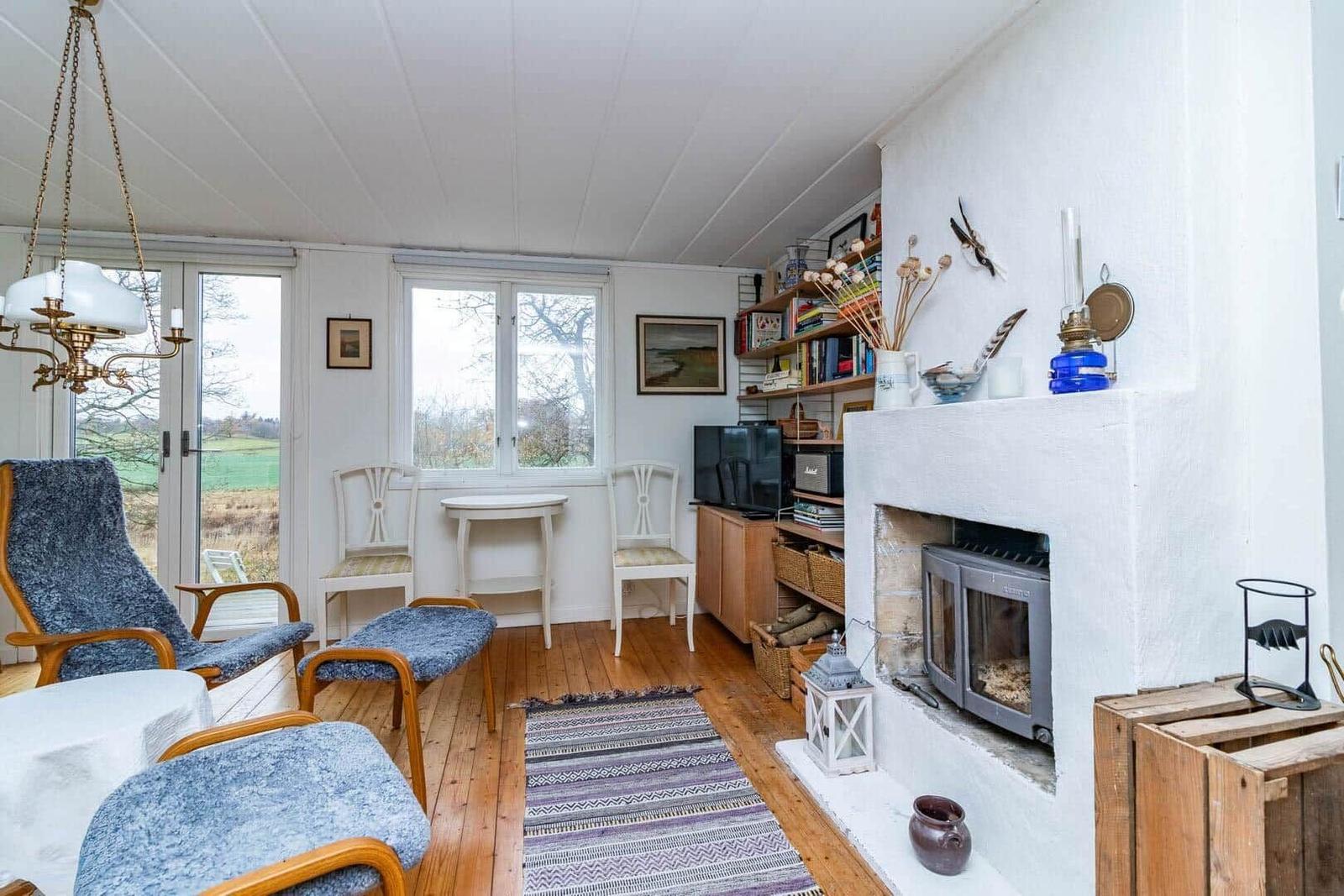 Wohnzimmer mit Kamin, Fenstern und Holzboden. Möbel und Dekoration sind sichtbar.