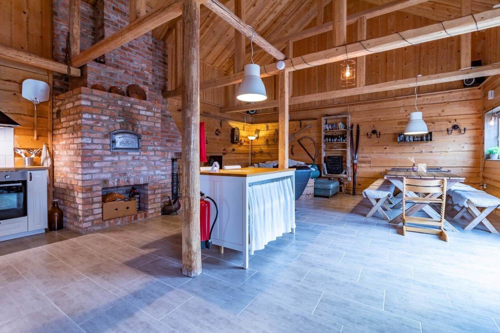 Großer Raum mit Holzdecke, Kamin und Küchenbereich mit Tisch und Stühlen.