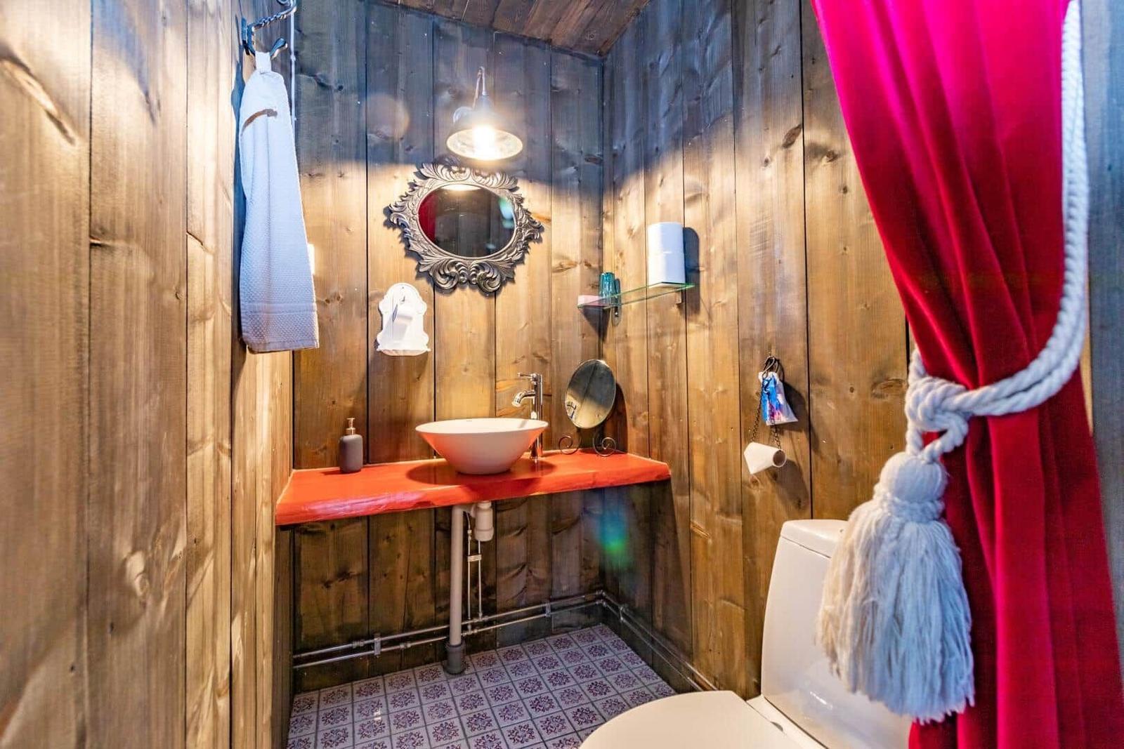 Badezimmer mit Holzwand, Waschbecken auf roter Oberfläche und roter Vorhang.