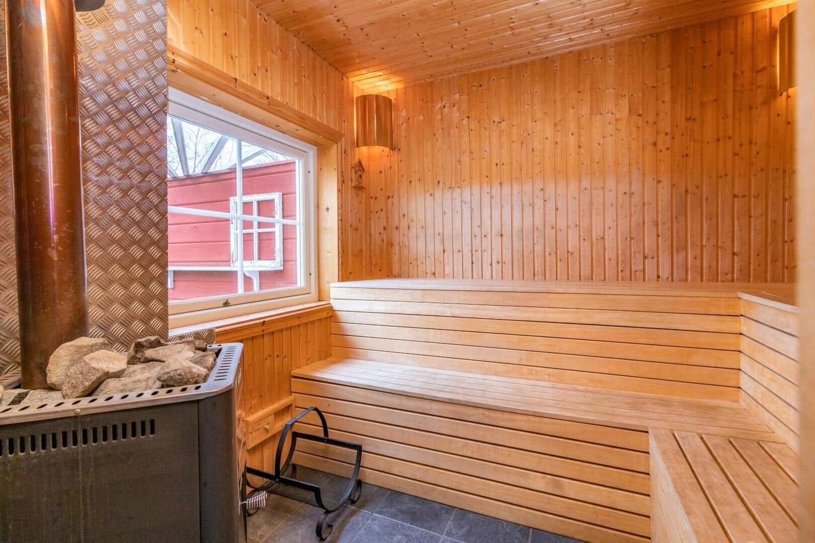 Sauna mit Holzbank, Kaminofen und Fensterblick auf roten Holzaufbau.