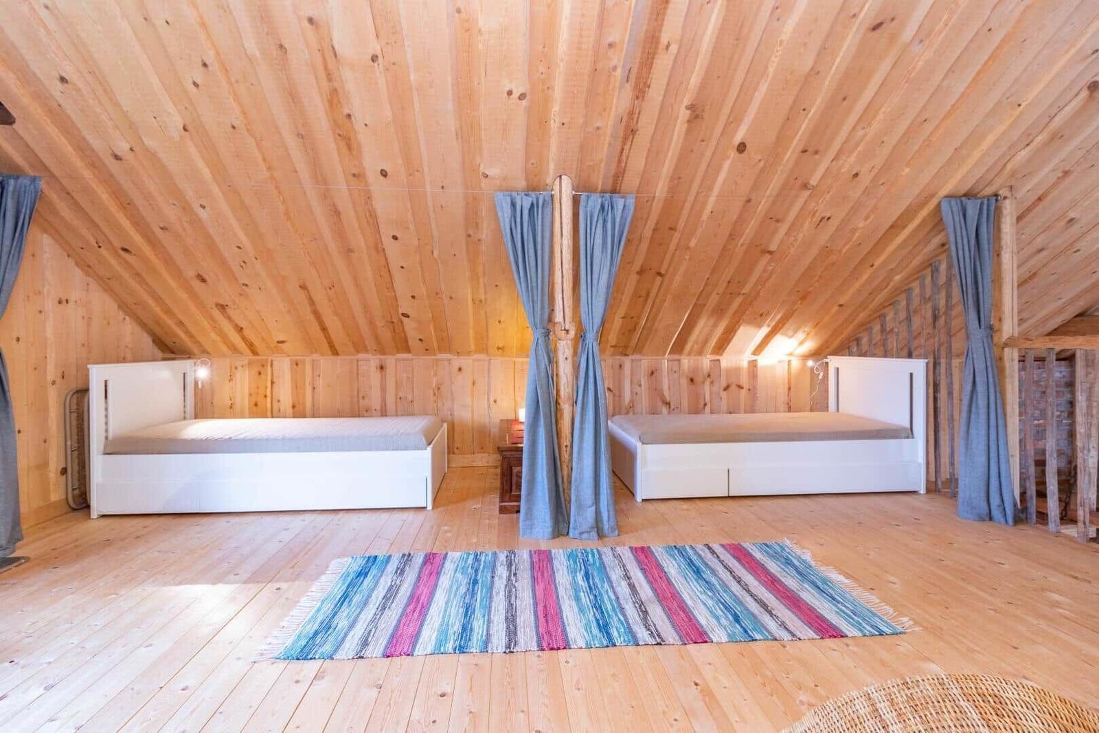 Zwei Betten in einem Dachgeschosszimmer mit Holzdecke und Boden. Ein buntes Teppich liegt im Zentrum.