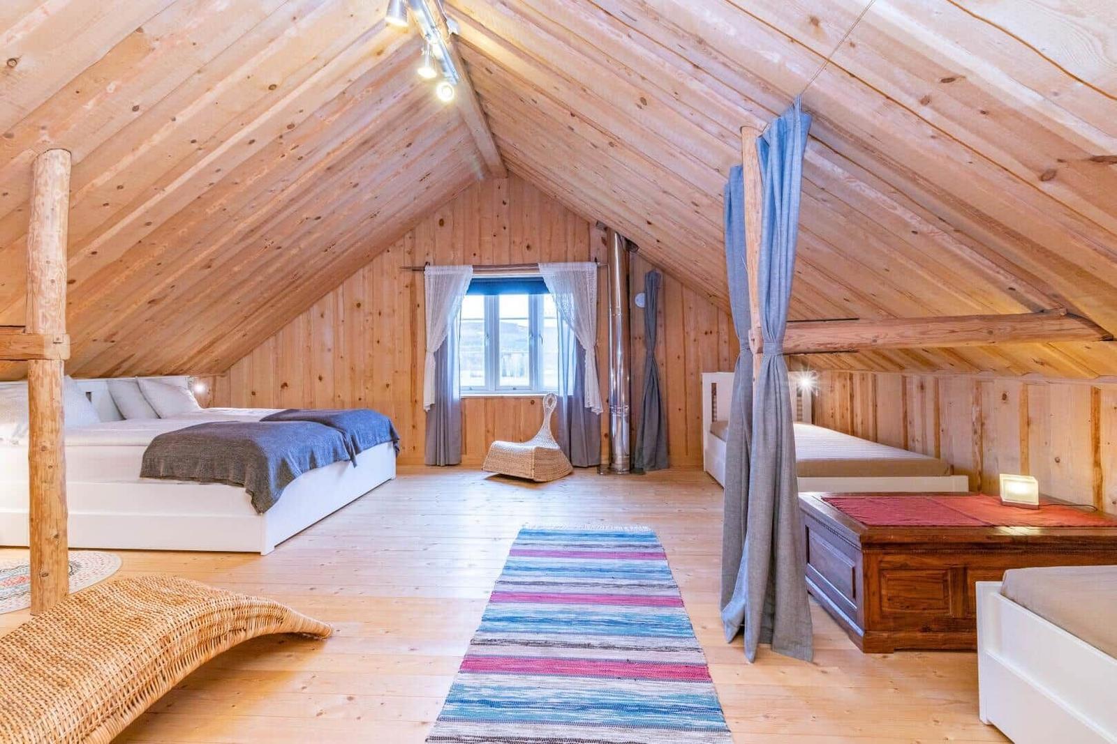 Dachgeschosszimmer mit Holzwand, zwei Betten und einem Fenster.