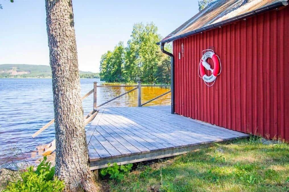 Rotes Holzhaus am See mit hölzerner Terrasse und Rettungsring an der Wand.