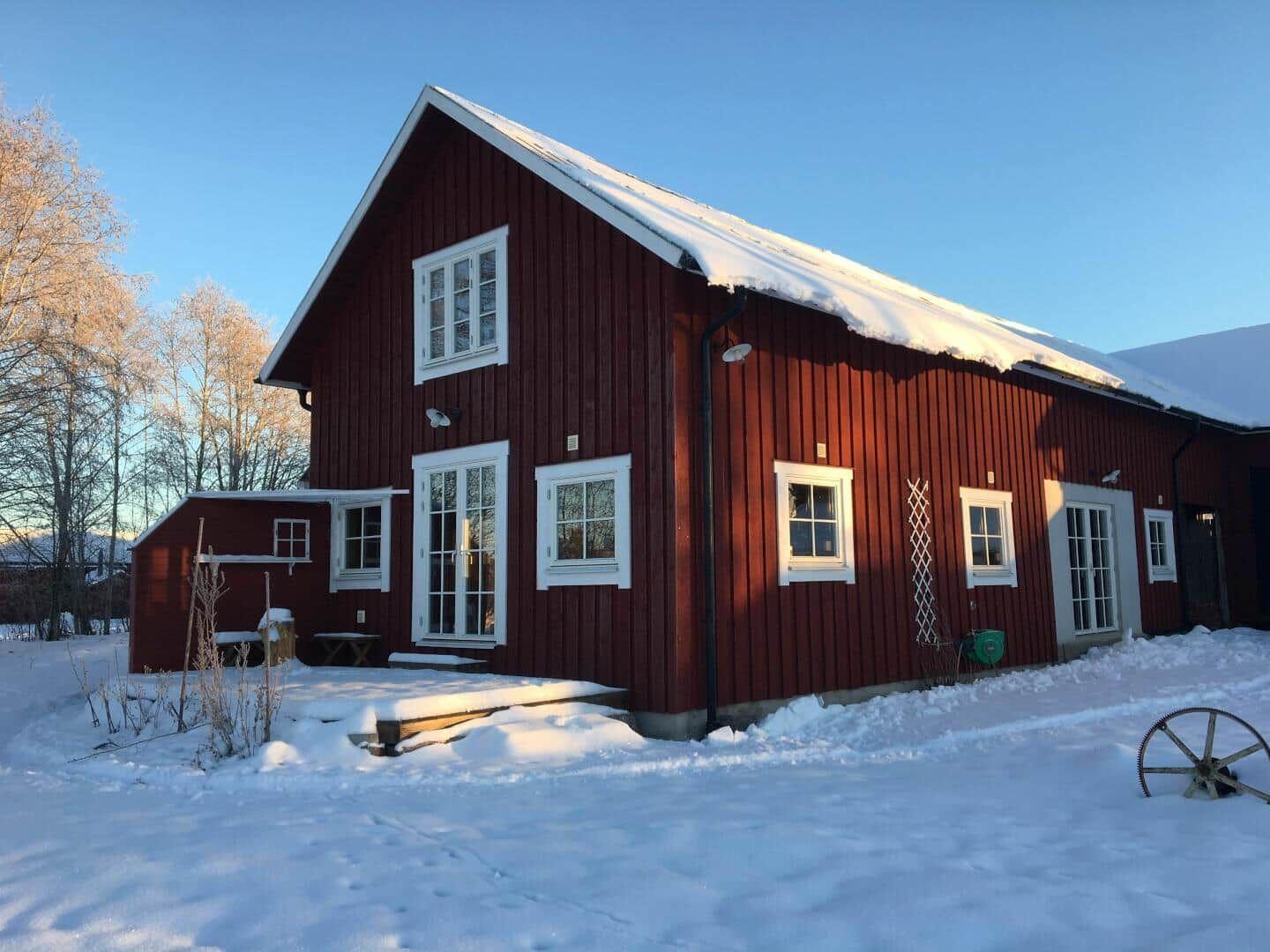Rotes Holzhaus mit Schneebedecktem Dach und weißen Fensterrahmen im Winter.
