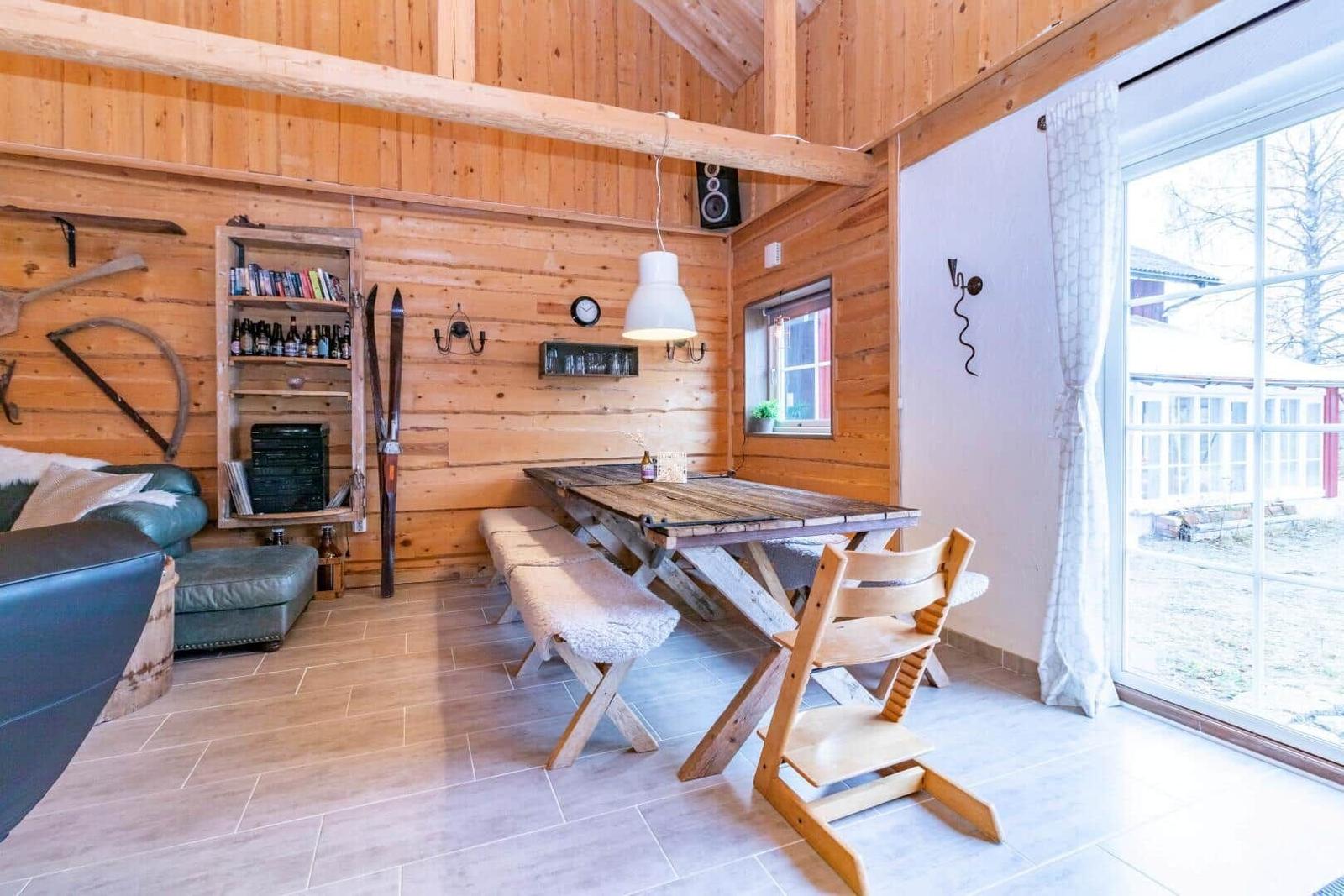 Essbereich mit Holztisch, Bänken und Stuhl. Holzwände, Fenster und Tür.
